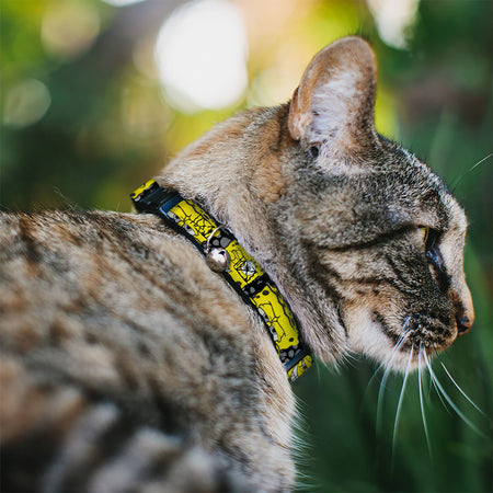Side profile of a tabby cat wearing a bright yellow patterned collar with a bell, looking right. Green background.